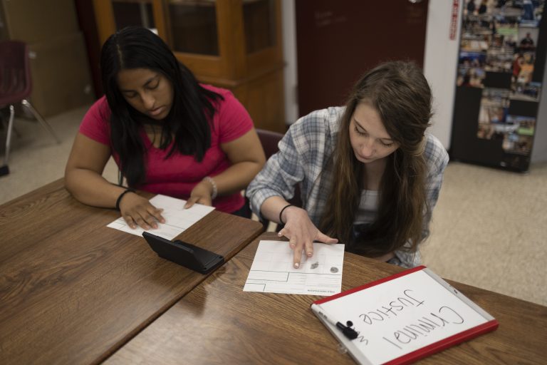Two students seated at desk studying a paper.