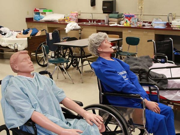 Two CPR mannequins seated in wheel chairs.