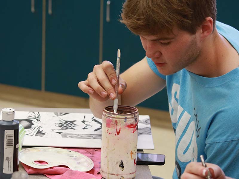 A student dipping brush in paint.