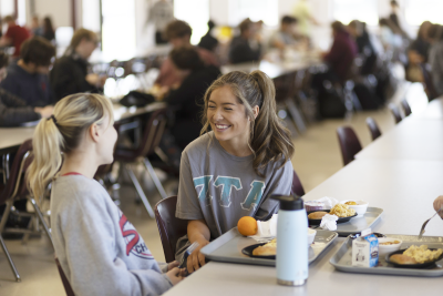 Two female students laughing at lunch table.