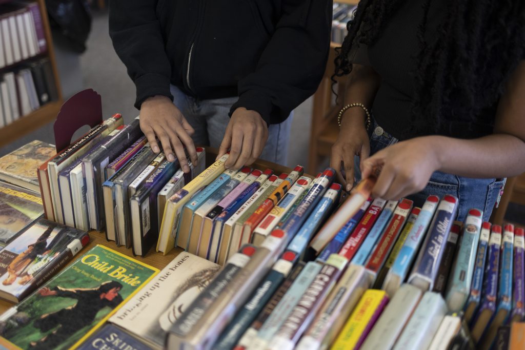 Two students browse books placed on a table.