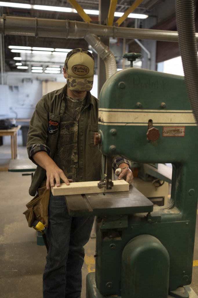 A student using a band saw to cut wood.